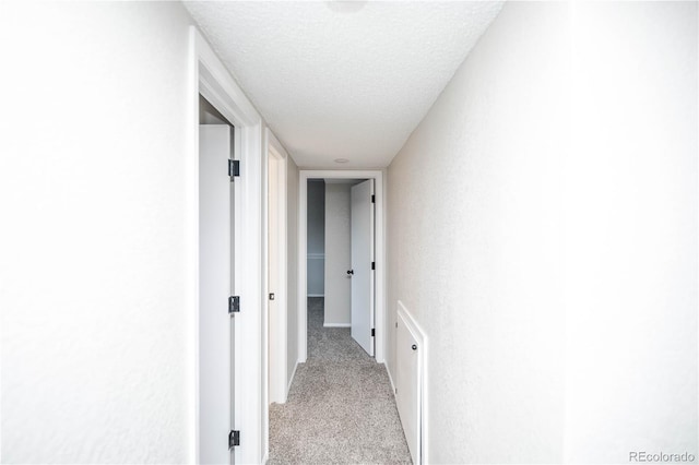 hall featuring a textured ceiling and light colored carpet