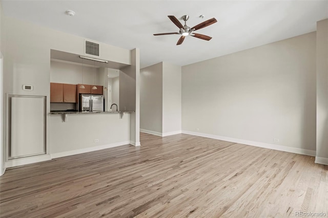 unfurnished living room featuring ceiling fan, sink, and light wood-type flooring