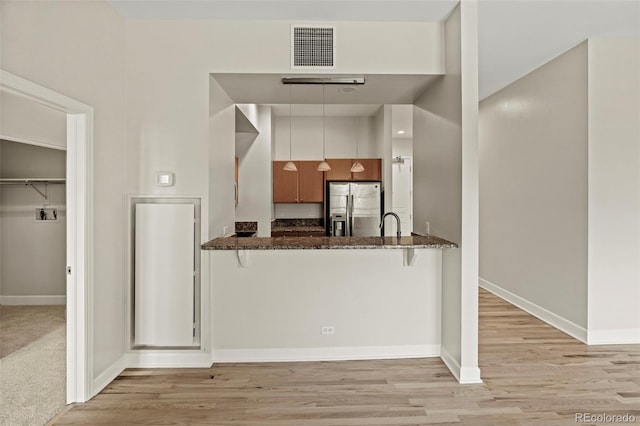 kitchen with kitchen peninsula, white cabinetry, dark stone counters, and stainless steel fridge with ice dispenser