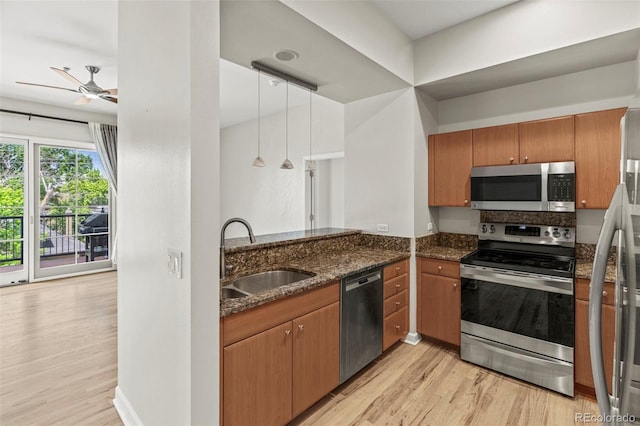 kitchen featuring hanging light fixtures, appliances with stainless steel finishes, dark stone countertops, light hardwood / wood-style floors, and sink