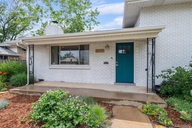 5315 Newland St, Arvada, CO 80002 - property entrance featuring a chimney, brick siding, and covered porch