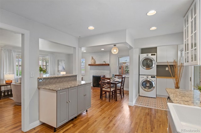 5315 Newland St, Arvada, CO 80002 - kitchen featuring stacked washer and clothes dryer, light wood-style floors, glass insert cabinets, a fireplace, and white cabinets