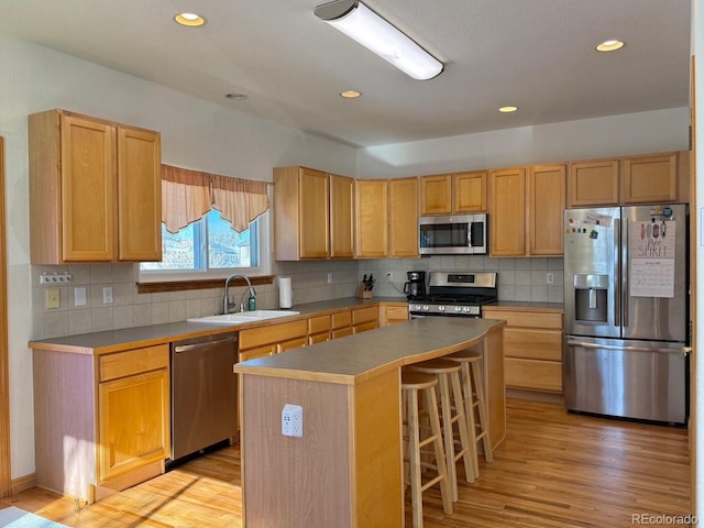 kitchen with a kitchen island, sink, a breakfast bar area, stainless steel appliances, and light wood-type flooring