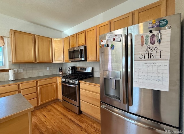 kitchen with appliances with stainless steel finishes, decorative backsplash, and light hardwood / wood-style flooring