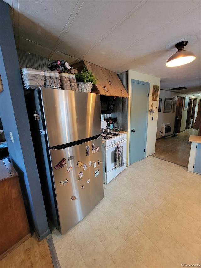 kitchen with premium range hood, white gas range, heating unit, and stainless steel refrigerator