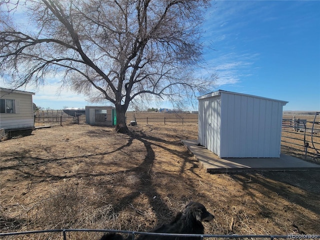 view of yard featuring an outbuilding, a rural view, fence, and a shed