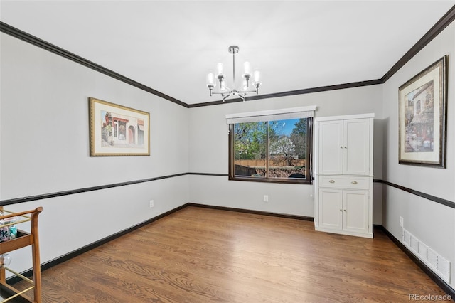 spare room with crown molding, visible vents, wood finished floors, and a chandelier