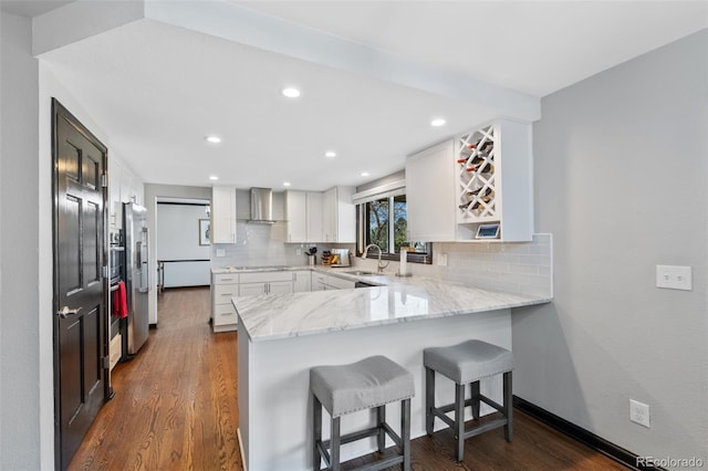 kitchen featuring tasteful backsplash, light stone counters, a peninsula, dark wood-style floors, and wall chimney exhaust hood