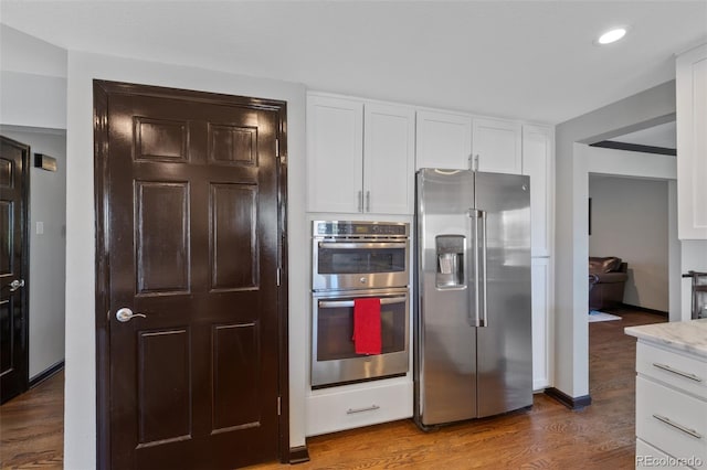 kitchen with appliances with stainless steel finishes, light stone countertops, wood finished floors, white cabinets, and recessed lighting