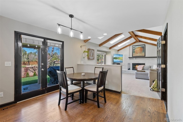dining space featuring lofted ceiling with beams, a brick fireplace, wood finished floors, and a wealth of natural light