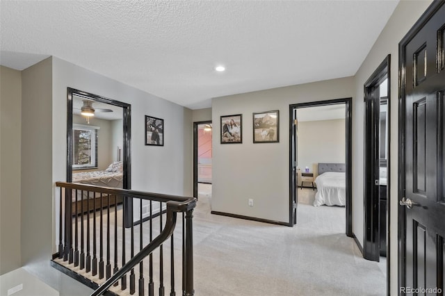 corridor featuring a textured ceiling, light colored carpet, baseboards, an upstairs landing, and recessed lighting