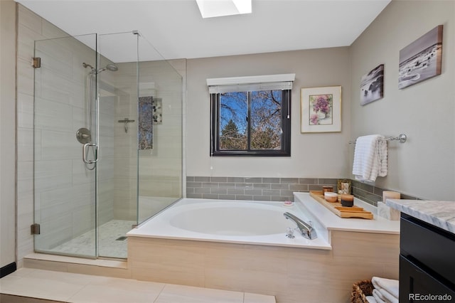 bathroom featuring a skylight, a shower stall, a garden tub, and vanity