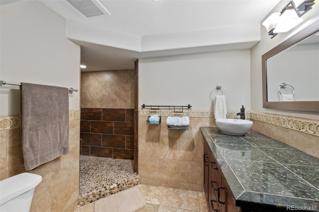 bathroom with vanity, walk in shower, toilet, and tile walls