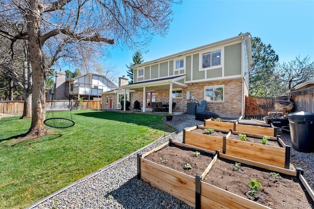 rear view of house featuring brick siding, a vegetable garden, a fenced backyard, a patio area, and a yard