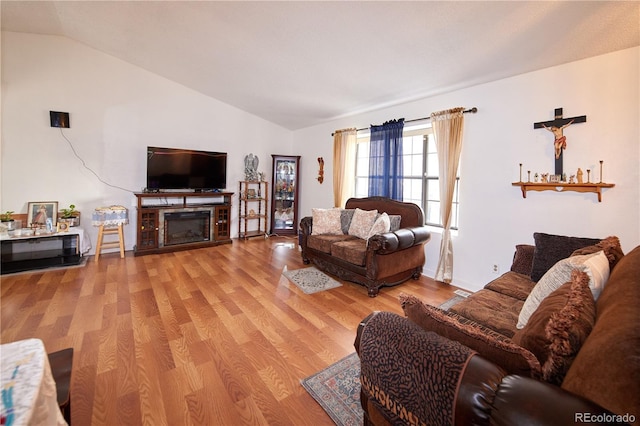 living room with a glass covered fireplace, light wood finished floors, and lofted ceiling