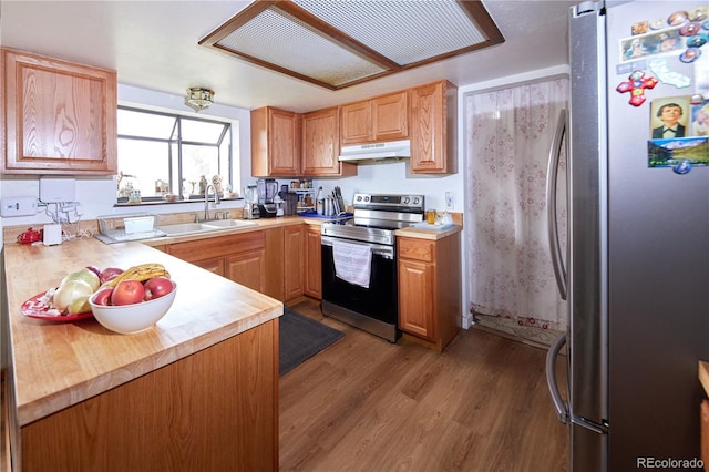 kitchen featuring dark wood-style flooring, light countertops, under cabinet range hood, a sink, and appliances with stainless steel finishes