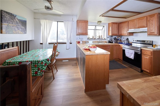 kitchen with ceiling fan, stainless steel electric range, light countertops, under cabinet range hood, and a wealth of natural light