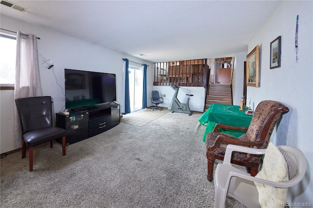 living room featuring carpet flooring, stairs, a textured ceiling, and visible vents