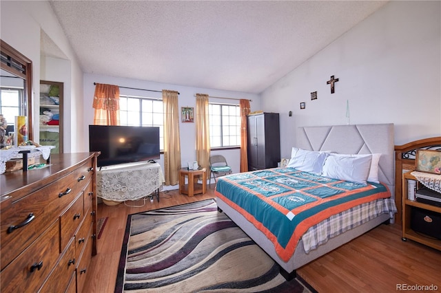 bedroom with a textured ceiling, wood finished floors, and lofted ceiling