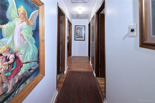 hallway featuring a textured ceiling, attic access, baseboards, wood finished floors, and visible vents
