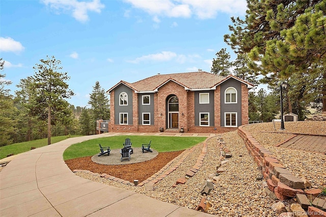 colonial inspired home with a tiled roof, a fire pit, brick siding, and a front yard