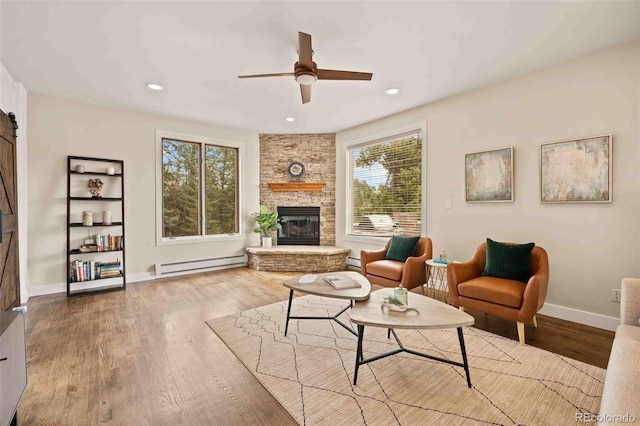 living area with a ceiling fan, wood finished floors, a fireplace, baseboards, and a baseboard radiator