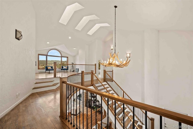 hall with vaulted ceiling with skylight, wood finished floors, a chandelier, and an upstairs landing
