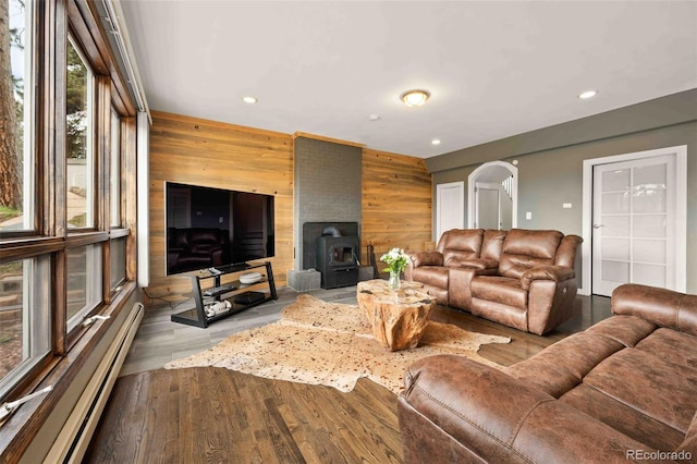 living room featuring a wood stove, wood walls, recessed lighting, wood finished floors, and a baseboard heating unit