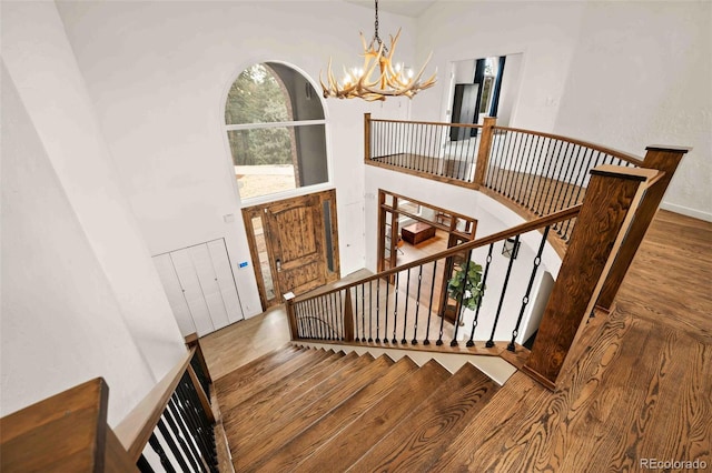 stairway featuring baseboards, a high ceiling, a notable chandelier, and wood finished floors