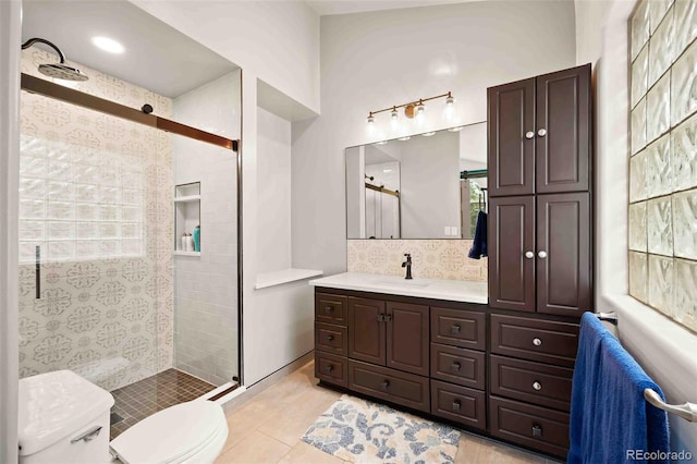 bathroom featuring vanity, tile patterned flooring, toilet, tasteful backsplash, and a tile shower