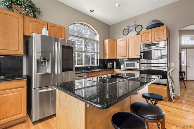 kitchen with dark stone countertops, appliances with stainless steel finishes, a center island, and backsplash