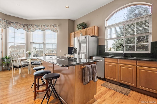 kitchen featuring appliances with stainless steel finishes, a breakfast bar, sink, a center island, and light wood-type flooring