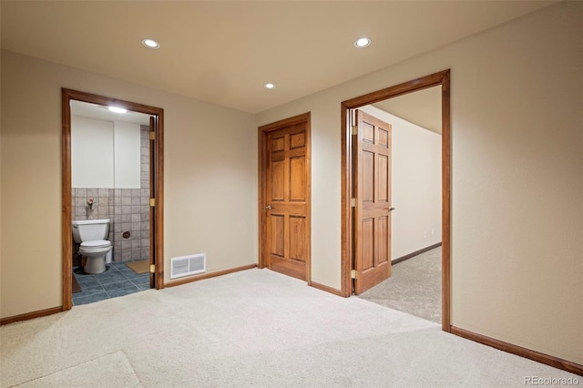 unfurnished bedroom featuring ensuite bathroom, light colored carpet, and tile walls