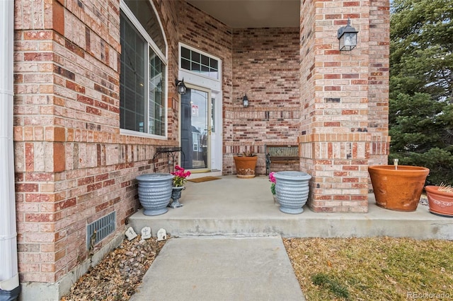 doorway to property featuring covered porch, brick siding, and visible vents