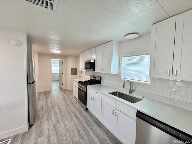 8480 Adams Way, Denver, CO 80229 - kitchen with stainless steel appliances, white cabinets, backsplash, light wood finished floors, and healthy amount of natural light