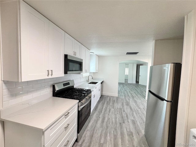 8480 Adams Way, Denver, CO 80229 - kitchen with appliances with stainless steel finishes, arched walkways, decorative backsplash, light wood-type flooring, and white cabinetry