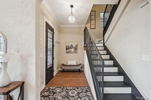 foyer entrance featuring baseboards, a textured wall, ornamental molding, wood finished floors, and stairs