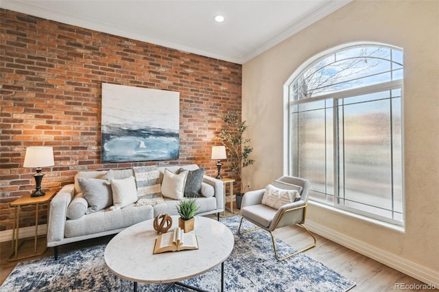 living room with brick wall, crown molding, baseboards, and wood finished floors