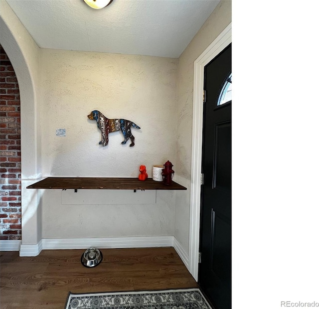 foyer entrance featuring baseboards, a textured ceiling, arched walkways, and wood finished floors