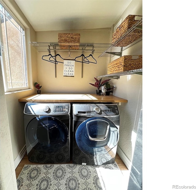 clothes washing area with laundry area, washer and clothes dryer, baseboards, and wood finished floors