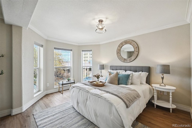 bedroom featuring a textured ceiling, ornamental molding, wood finished floors, and baseboards