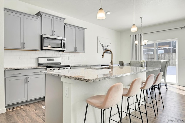 kitchen featuring appliances with stainless steel finishes, sink, light stone countertops, a center island with sink, and decorative backsplash