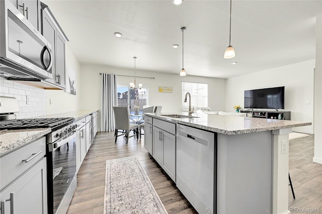 kitchen with a sink, stainless steel appliances, decorative backsplash, light stone countertops, and a notable chandelier