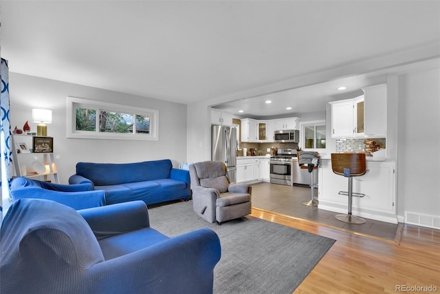 living room with recessed lighting, visible vents, and wood finished floors