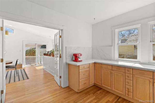 kitchen featuring tasteful backsplash, light countertops, vaulted ceiling, and light wood finished floors