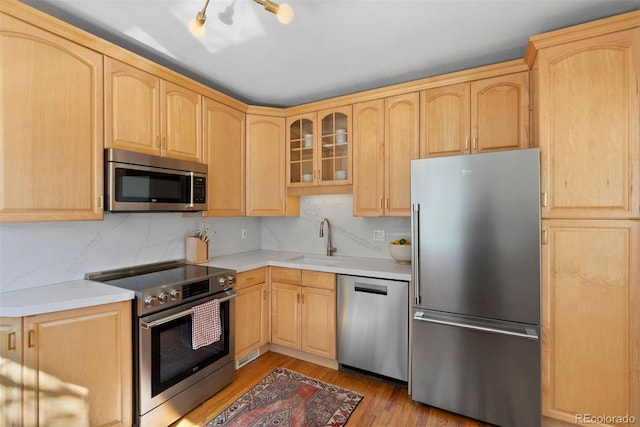 kitchen with light brown cabinetry, appliances with stainless steel finishes, a sink, and glass insert cabinets