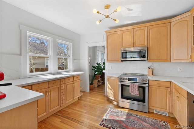 kitchen featuring a chandelier, light countertops, appliances with stainless steel finishes, light brown cabinetry, and light wood finished floors