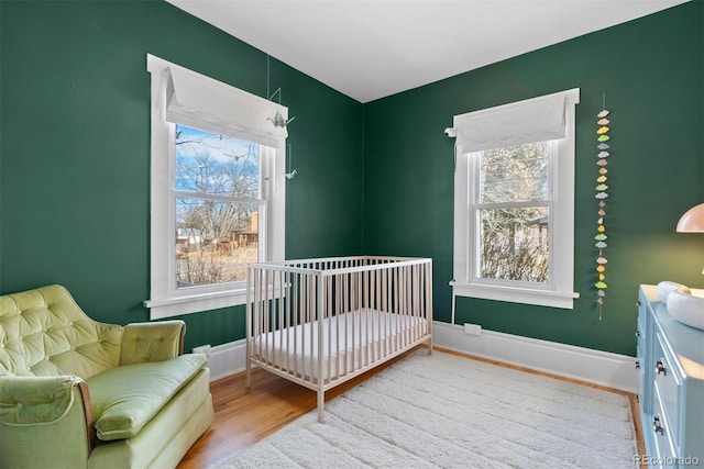 bedroom featuring a nursery area, wood finished floors, and baseboards