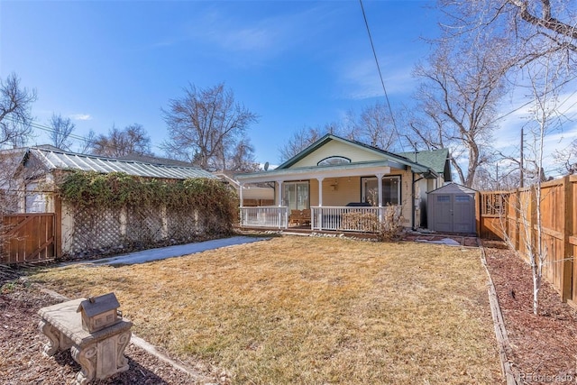 rear view of property featuring a porch, a fenced backyard, an outdoor structure, a lawn, and a shed