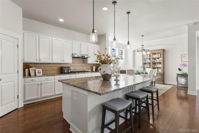 kitchen with dark wood finished floors, under cabinet range hood, decorative backsplash, white cabinets, and a kitchen island